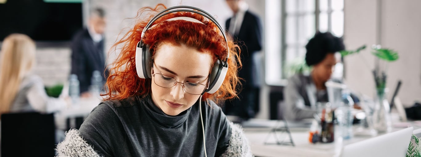 Kvinne med rødt hår lytter på musikk mens hun jobber. Foto