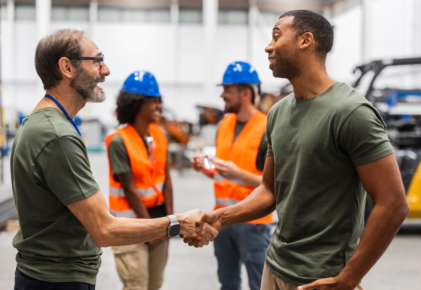 To ansatte håndhilser, to andre i bakgrunnen. Foto