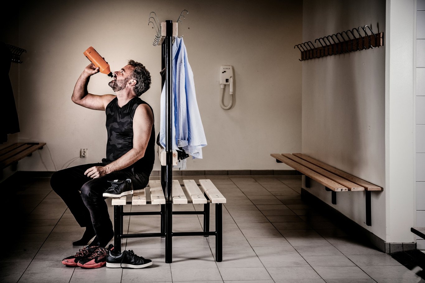 Mann i garderobe drikker fra vannflaske. Foto