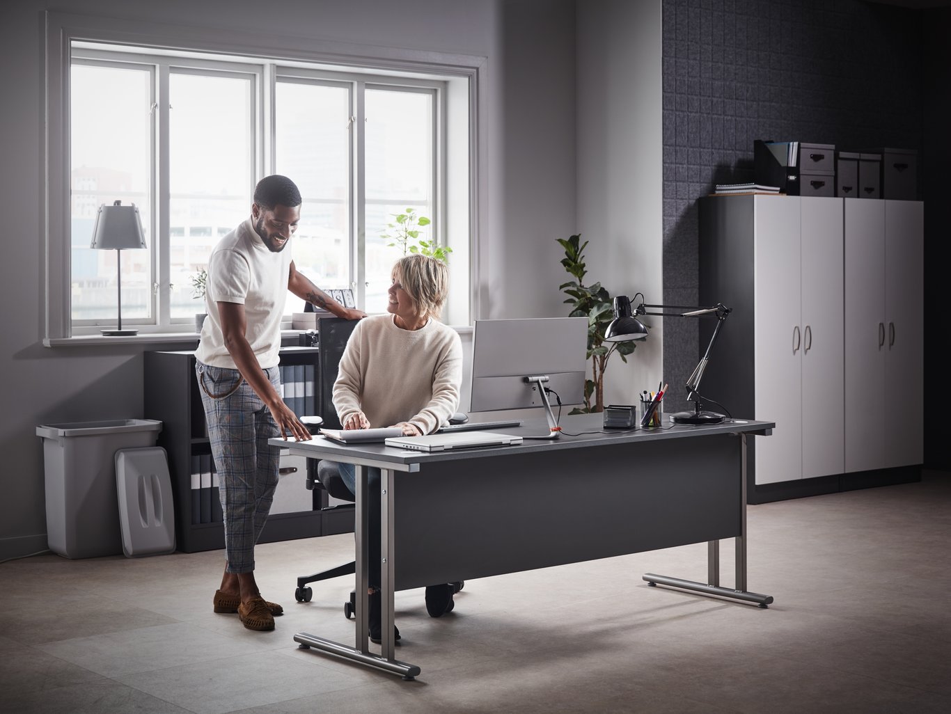 Mann og kvinne snakker sammen ved kontorpult. Foto