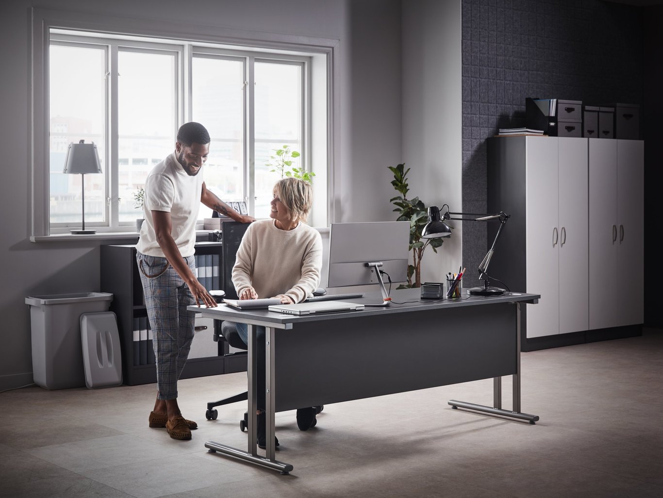 Mann og kvinne snakker sammen ved kontorpult. Foto