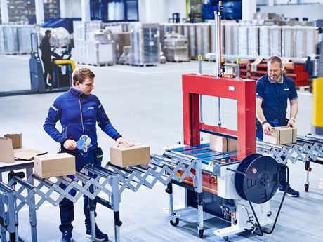 To menn ved stroppemaskin fra Cowan på lager. Foto